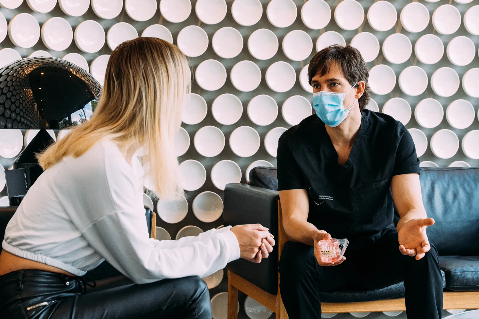 A masked dentist and patient discuss treatment in the Maida Smiles consultation lounge.