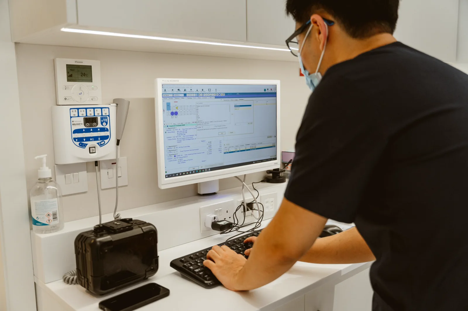 A dentist reviews treatment records on a monitor in a bright clinic room.