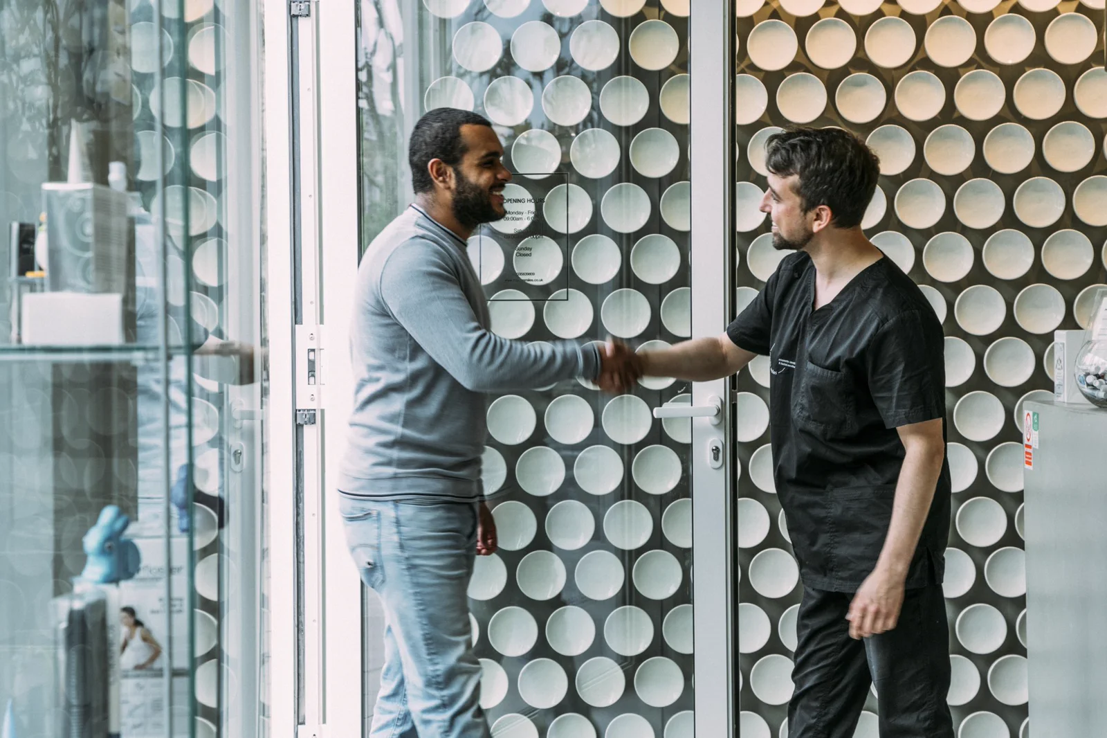 A dentist greets a patient warmly at the clinic entrance.